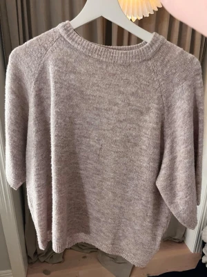 Beige stickad tröja från 157 XS - Mysig stickad tröja i beige ton från 157, storlek XS. Tröjan har rund halsringning med ribbad kant och halvlånga ärmar. Perfekt för lager-på-lager och chill dagar. Materialet är mjukt och ger en skön känsla mot huden.