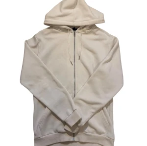 Vit/Beige hoodie med dragkedja från SMOG - Zara - Vit/beige hoodie från SMOG köpt i ZARA i slim fit med huva och snörning. Tröjan har dragkedja framtill, två fickor och ribbade muddar vid ärmslut och nederkant. Tillverkad i mjuk bomull, perfekt för chill dagar. Storlek L passar även storlek M modellen är slim fit.