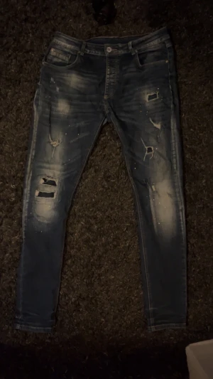 Dondup liknande jeans - Säljer ett par blå jeans med coola slitningar och detaljerade hål på framsidan. normal passform och klassisk femficksdesign. Färgskiftningar och tvättade partier ger en snygg streetkänsla. Perfekt för dig som gillar en edgy stil. För mer frågor kontakta gärna//VMresell