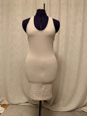 Beige ärmlös klänning H&M Divided - En enkel och stilren beige klänning från H&M Divided. Modellen är ärmlös med v-ringning och har en kroppsnära passform. Klänningen är tillverkad i mjuk bomull och passar perfekt för en clean och avslappnad look.