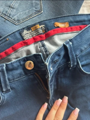 Mörkblå denimshorts med rosett - Snygga mörkblå denimshorts från Stouse Denim i skinny fit. Klassisk femficksdesign, låg midja och uppvikta ben. Baksidan har en söt rosettdetalj på fickan. Guldknapp och dragkedja framtill. Perfekta för sommaren och chill dagar. 