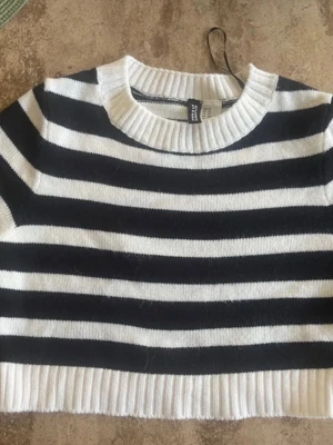 Randig croppad tröja från H&M Divided - Snygg croppad stickad tröja från H&M Divided i storlek XS. Tröjan har breda svarta och vita ränder, rund hals och ribbade muddar vid hals och nederkant. Perfekt för dig som gillar en chill och trendig stil.