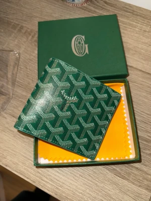 Grön lyxig plånbok med mönster - Snygg grön plånbok från G med deras ikoniska grafiska mönster på utsidan. Plånboken är i skinn och har flera kortfack samt plats för sedlar. Perfekt accessoar för dig som vill sticka ut med något exklusivt och stilrent.