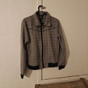 Rutig bomberjacka LCEE - Snygg rutig bomberjacka från LCEE Limited Edition med svart dragkedja och krage. Jackan har svart kant vid ärmslut och nederkant, samt diskret metallmärke på baksidan. Perfekt för dig som gillar klassisk stil med en modern twist..  Nytt med lappen kvar. Jag kan inte se några hål eller skador etc. Även om de är nytt.  Obs! Jag står inte för frakbolagets slarv, skador eller annat som händer efter att jag har postat.