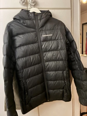 Svart dunjacka Peak Performance M - Svart dunjacka från Peak Performance i storlek M. Jackan har huva, quiltad design och dragkedja framtill. Perfekt nu under vintern, pris kan diskuteras!