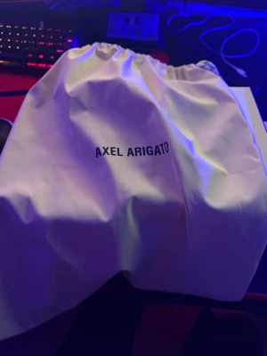 Svarta sneakers från Axel Arigato - Säljer ett par svarta sneakers från Axel Arigato med klassisk rund tå och platt vit sula. Skorna har snörning och är tillverkade i skinn, vilket ger en clean och stilren look. Perfekt för dig som gillar minimalistisk design och vill ha ett par snygga sneakers.