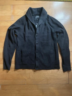 Hollister kofta - Riktigt snygg stickad kofta med tryck på ryggen från Hollister. Koftan är i bra skick utan några synliga defekter, även om spår av användning finns. Storlek L 