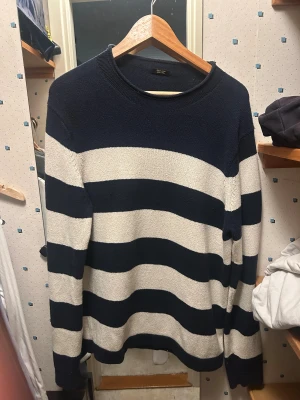 Randig Tröja - Säljer en snygg stickad tröja från Massimo Dutti i exklusiv bomull. Tröjan har breda marinblå och vita ränder, rund hals och långa ärmar. Perfekt för dig som gillar klassisk stil med en modern twist. Passar till jeans eller chinos.