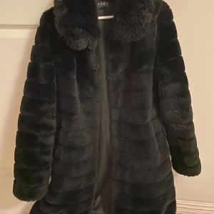 Svart faux fur från Jones New York - Säljer en svart pälsjacka från Jones New York i storlek M. Jackan har en fluffig krage, horisontella ränder och stängs med diskreta knappar framtill. Perfekt för dig som vill ha en snygg och varm look under kyliga dagar.
