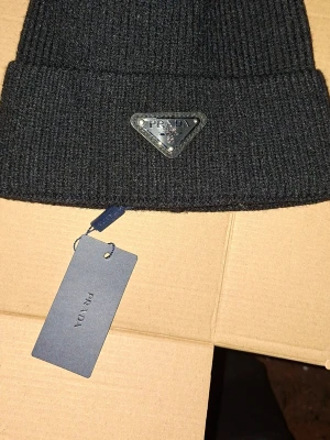 Svart stickad väst från Prada - Snygg svart stickad väst från Prada med klassisk ribbad design och ikonisk logotyp framtill. Västen har en enkel och stilren form som passar till många olika outfits. Perfekt för dig som gillar exklusiva märken och vill ha en cool detalj i garderoben. PRISLAPPEN ÄR BORTRA MEN DUSTBAGEN ÄR KVAR