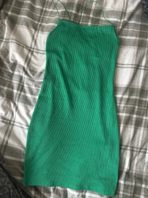 Grön ribbad klänning från H&M Divided - Snygg grön ribbad klänning från H&M Divided i storlek S. Klänningen har smala axelband som korsas i ryggen och är figurnära med kort längd. Perfekt för dig som gillar enkel och stilren design med en färg som verkligen poppar.