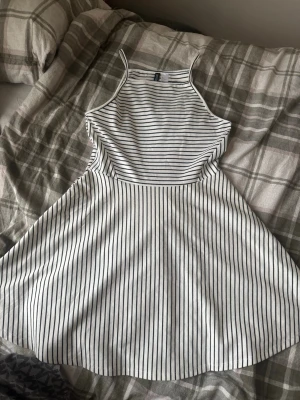Randig sommarklänning från H&M Divided - Säljer en vit och svart randig klänning från H&M Divided i storlek 42. Klänningen har smala axelband och är ärmlös med en utställd kjol. Perfekt för varma dagar och har en fräsch, ungdomlig stil. Materialet är mjukt och bekvämt bomull.