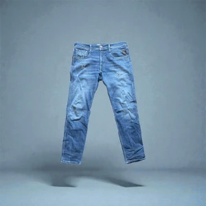 Replay Anbass - Säljer ett par snygga Replay Anbass jeans i slim fit med klassisk femficksdesign. Jeansen är blå med lätt slitna detaljer och har en skinnpatch med Replay-logga bak. Passformen är smal och materialet är slitstark denim i bomull.