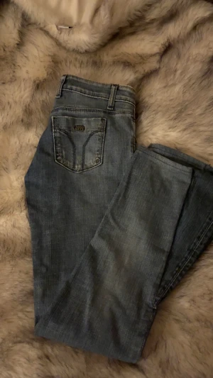 Miss Sixty blå jeans  - Snygga blå jeans från Miss Sixty med klassisk femficksdesign och smal passform. Jeansen har låg midja, subtila slitningar och detaljerade sömmar på bakfickorna. Perfekt för dig som gillar en stilren och modern look. Omsydda till bootcut 