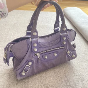 Lila city väska 💜 - Säljer en ikonisk lila handväska i skinn med silverfärgade detaljer. Man får även med ett längre band så man kan ha den över axeln 💜intressekoll så tryck inte på köp