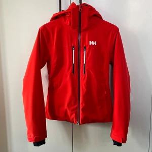 Röd skidjacka Helly Hansen Alphelia Lifaloft - Säljer min favoritjacka från Helly Hansen då den tyvärr har blivit för liten för mig som brukar ha S eller M i jackor. Nypris ca 5000, finns inte längre att köpa ny i denna färg. Lite naturligt slitage (kom privat för fler bilder) men annars fint skick. Storlek XS. Nytvättad.