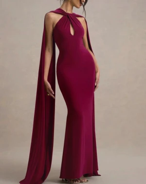 Vinröd långklänning med cape - Säljer en vinröd långklänning med cape-detalj och snygg cutout framtill. Klänningen är figurnära med ärmlös design och har en elegant, dramatisk look. Perfekt för bal eller fest. Materialet känns mjukt och följsamt mot kroppen.