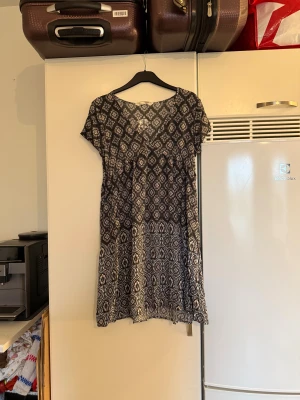 Svart mönstrad kortklänning Odd Molly - Supersöt kortklänning från Odd Molly med svart botten och vitt blommigt mönster. Klänningen har v-ringning, korta ärmar och ett flowigt fall. Perfekt för dig som gillar boho-vibe och vill ha något bekvämt och snyggt. Materialet är mjukt och lätt, troligen bomull. Från märket Odd Molly. Storlek 2 som enligt deras storleksguide motsvarar en M. Mycket fint skick, jag hittar inga synliga anmärkningar eller defekter.  