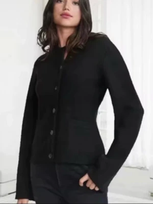 Svart stickad kofta med knappar - Säljer en svart stickad kofta med rund hals och stora knappar framtill. Koftan har lång ärm och ribbade muddar vid ärmslut och nederkant. Enkel och stilren modell som passar till mycket.