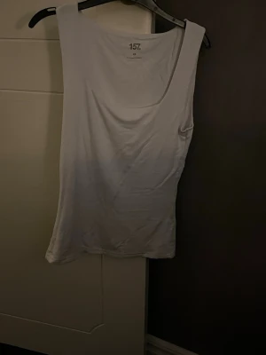 Vit ärmlös linnetopp från 157 - En basic vit linnetopp från 157 med rund halsringning och ärmlös design. Perfekt att styla till jeans eller shorts under varma dagar. Tillverkad i mjuk bomull som känns skön mot huden.