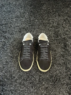 Svarta Saint Laurent sneakers i mocka - Säljer nu ett par sjuka snygga Saint Laurent Skor! Skicket är vädligt fint förutom att sulan har släppt en aning. Priset är inte hugget i sten vid snabb affär☺️ Inget tillbehör medföljer. Hör gärna av er om ni har fler frågor!