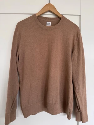 Beige stickad tröja från GAP - Säljer en enkel och snygg beige stickad tröja från GAP i storlek M. Tröjan har rund hals, långa ärmar och ribbade muddar vid hals, ärmslut och nederkant. 