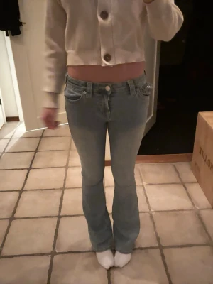 Ljusblå bootcut jeans låg midja - Säljer ett par ljusblå jeans med snygg bootcut och låg midja. Jeansen har klassisk femficksdesign, knapp och dragkedja framtill. Materialet är jeans och passformen är normal med lätt utsvängda ben. Perfekt för dig som gillar retrovibbar och avslappnad stil.