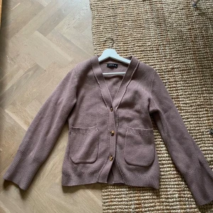 Beige kofta från Floreya med knappar - Säljer en beige stickad kofta från Floreya i storlek XS. Koftan har v-ringad hals, tre knappar framtill och två praktiska fickor. Materialet är mjukt och ribbat vid muddar och hals. Perfekt för lager-på-lager under kyliga dagar.