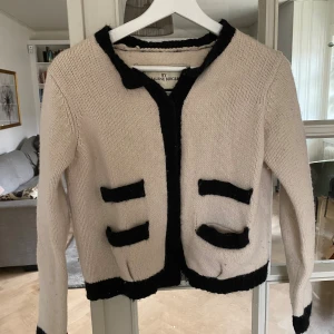 Beige stickad kofta från By Malene Birger - Säljer en beige stickad kofta från By Malene Birger med svarta kontrastdetaljer vid kanter och fickor. 