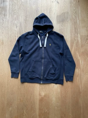 Polo Ralph Lauren zip - Säljer nu denna väldigt fina Polo Ralph Lauren tröjan då den inte passade. En klassisk marin blå zip tröja med vita snören och gult Ralph Lauren märke vilket gör den fantastiskt snygg. Den passar till i princip allt. Material🧵65% bomull och 35% polyester Skick 8/10 Storlek✅ L Skickar alltid samma dag. Hör av er vid frågor