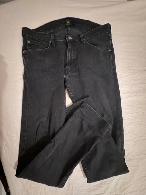 Svarta Lee Luke jeans W34 L32 - Säljer ett par svarta Lee Luke jeans i klassisk femficksmodell. Jeansen har raka ben, normal passform och snygga detaljer med Lee-logga på knappen och bakfickan. Materialet är mjukt denim i bomull med en mörk tvätt.