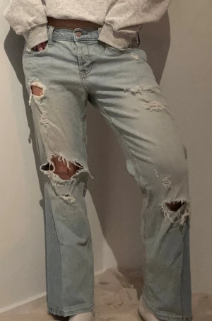Ljusblå ripped jeans med straight fit - Säljer ett par ljusblå jeans med flera slitningar och hål på benen för en edgy vibe. Midjemått rakt över: 40 cm Innerbenslängd: 68 cm