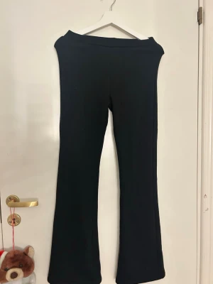 Svarta bootcut byxor från Kappahl - Svarta bootcut byxor från Kappahl i storlek 164. Byxorna har en mjuk insida och är tillverkade i ett stretchigt material som känns skönt mot huden. De har hög midja och en klassisk bootcut passform som ger en snygg siluett.