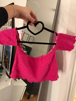 Rosa croppad offshoulder topp - Säljer en superfin rosa croppad topp med offshoulder ärmar från Zara Trafaluc. Toppen har en smockad struktur och vågig kant nertill och vid ärmarna. Perfekt för sommarens alla tillfällen och ger en riktigt söt vibe.