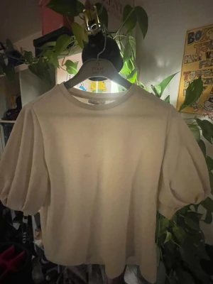 Vit puffärm t-shirt från KappAhl - Säljer en enkel vit t-shirt från KappAhl i storlek M. T-shirten har puffiga korta ärmar och rund halsringning. Materialet känns mjukt och bekvämt, perfekt för en clean och avslappnad look.(tar bara swish)