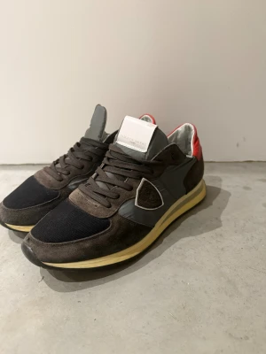 Philippe Model  - Snygga sneakers från Philippe Model i brunt mocka och textil med grå detaljer och röd häl. Skorna har snörning, svart mesh framtill och gul/beige sula. Perfekta för dig som vill ha en unik och sportig look.