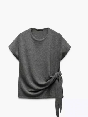 Grå topp med knyt från Zara - Jätte söt  topp från Zara med korta ärmar och rund halsringning. Toppen har en söt knytdetalj i sidan som ger en unik look. Perfekt att matcha med jeans eller kjol för en stilren vibe.🩷🩷🩷