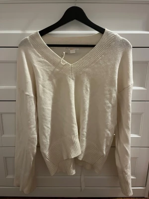 Vit stickad tröja från Gina Tricot - Mysig vit stickad tröja från Gina Tricot med bred ribbad v-ringning och långa ärmar.