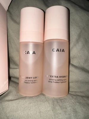 CAIA setting sprays duo - Två CAIA setting sprays i snygga frostadrosa flaskor med ljusrosa lock. Ena är 'That Dewy Lock' för glow och den andra 'That Extra Hydration' för extra fukt. 2 x 55 ml