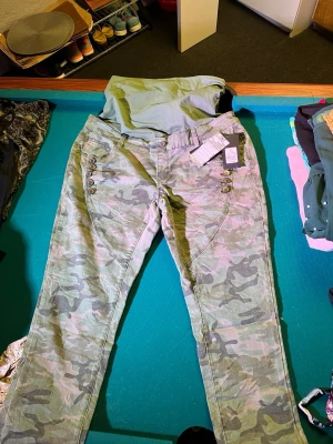 Camo jeansbyxor med knappar, strl 44 - Snygga camoflagemönstrade jeansbyxor från Heartbeats i gröna toner. Byxorna har coola knappdetaljer vid fickorna och klassisk femficksdesign. Perfekta för dig som gillar streetstyle och vill sticka ut lite extra. Materialet är slitstarkt jeans.