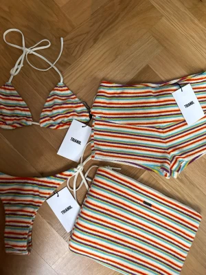 Randig bikini från Triangl - Färgglad bikini från Triangl med ränder i rött, blått, gult, orange och lila. Bikinin är i trekantsmodell. mjuk frotté. Medföljer en matchande necessär. Även shorts i samma mönster. Aldrig använd. Allt köptes för 2300kr. Xs i bikini och xxs i shorts