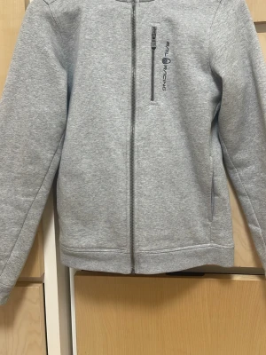 Grå zip hood från Sail Racing - Jag säljer då den inte kommer till användning ny pris 999kr och är köpt från Kidsbrand store jag ser inga fläckar på den och är i mycket bra skick har använt några gånger men är fortfarande mycket bra i skick