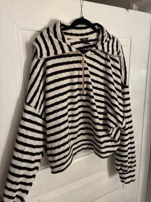 Randig tröja med dragkedja från Lindex - Supermysig tröja från Lindex i svart och vitt med horisontella ränder. Tröjan har en stor huva, lång ärm och en snygg dragkedja med ringdetalj framtill. Materialet är mjukt och känns lite som frotté. Perfekt för chill dagar eller när du vill vara extra bekväm.