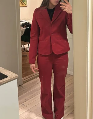 Röd kostym - Säljer en snygg röd kostym från Migel Stapper med kavaj och raka byxor. Kavajen har klassisk krage, tre knappar och fickdetaljer. Byxorna har normal passform och hällor för bälte. Ascool men den sitter lite tajt på mig