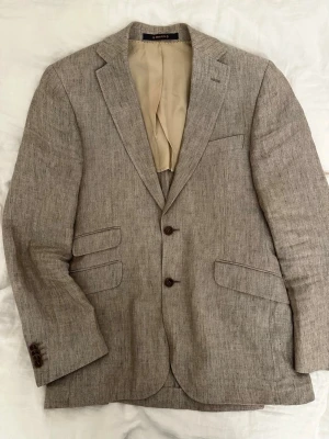 Beige linnékavaj från Morris, strl 46 - Säljer en snygg beige kavaj från Morris i 100% linne. Kavajen har klassisk passform, två knappar framtill, flera fickor och snyggt mönstrat innerfoder. Perfekt för dig som vill ha en stilren och luftig look till våren eller sommaren.