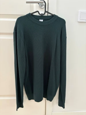 Mörkgrön stickad tröja DeFacto L - Säljer en mörkgrön stickad tröja från DeFacto i storlek L. Tröjan har rund halsringning, lång ärm och en ribbad struktur som ger en clean och stilren look. Perfekt för lager på lager under höst och vinter.