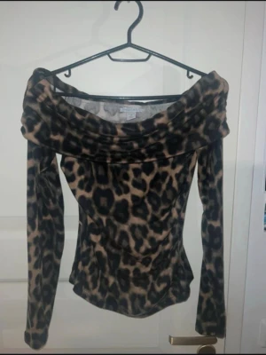 Leopardmönstrad offshoulder topp - Säljer en snygg offshoulder topp från amisu med leopardmönster i brun och svart. Toppen har långa ärmar och en bred, nedvikt krage. Använd 1 gång. 