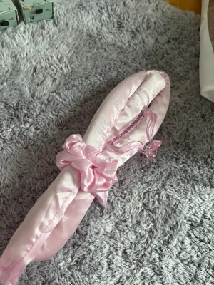 Ljusrosa satinväst med scrunchie-detalj - Säljer en ljusrosa väst i glansigt satinmaterial. Västen har en scrunchie-liknande detalj framtill och en mjuk, quiltad känsla. Perfekt för dig som gillar söta och trendiga accessoarer. Ingen synlig logga eller märke.