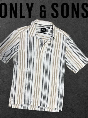 Randig skjorta från Only & Sons - Snygg kortärmad skjorta från Only & Sons med vertikala ränder i vitt, beige och svart. Skjortan har klassisk krage, knappar framtill och är gjord i ett lätt och luftigt linnematerial. Perfekt för en chill och stilren look.