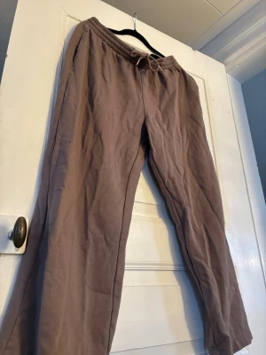 Bruna mjukisbyxor från H&M med snörning - Säljer ett par bruna mjukisbyxor från H&M i storlek M. Byxorna har elastisk midja med snörning och raka ben. Materialet är mjukt och skönt, perfekt för chill dagar. Fickor på sidorna för extra funktion. Snyggt basic-plagg att ha i garderoben. Passar S/M. Kommer även att sälja en tillhörande sweatshirt separat.